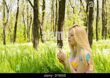 Schöne junge Frau bläst Blumensamen im grünen Feld den Wald. Stockfoto