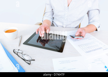 Erfolgreiche Geschäftsfrau am Schreibtisch sitzen und gleichzeitig mit modernen Geräten für Business-Kommunikation Stockfoto