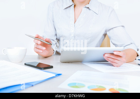 Entspannte Geschäftsfrau trägt lässige Hemd am Schreibtisch sitzen und arbeiten mit Daten auf digitale Tablet im Büro Stockfoto
