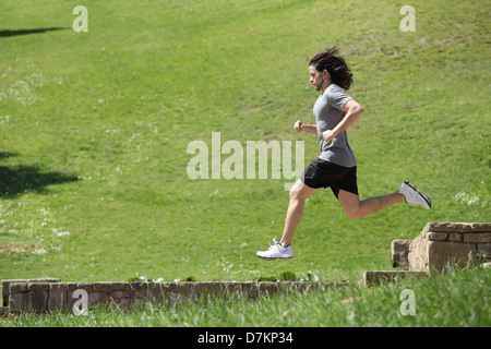 Sportler, laufen und springen in einem Park mit grünen Rasen im Hintergrund Stockfoto