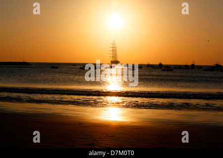 Silhouette eines großen Schiffes bei Sonnenuntergang in San Juan del Sur, Nicaragua. Goldenes Licht reflektiert das ruhige Meer, mit Booten am Horizont. Stockfoto