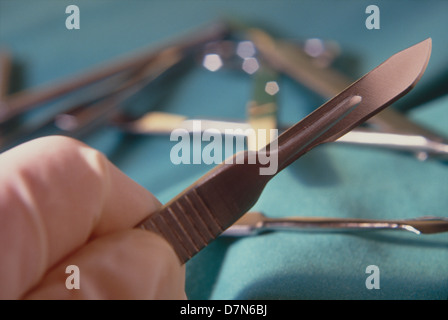 Ein Modell hält ein Skalpell mit chirurgischen Instrumenten im Hintergrund, © Mak Stockfoto