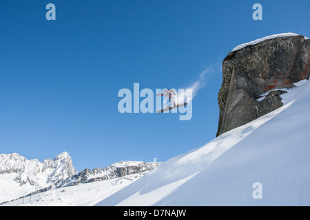 Snowboarder springt einem großen Felsen mit einem berühmten Chamonix-Hintergrund-Stil. Stockfoto