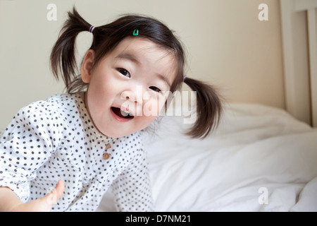 Korean American Kleinkind in Zöpfen lächelnd zu Kamera im Schlafzimmer Stockfoto