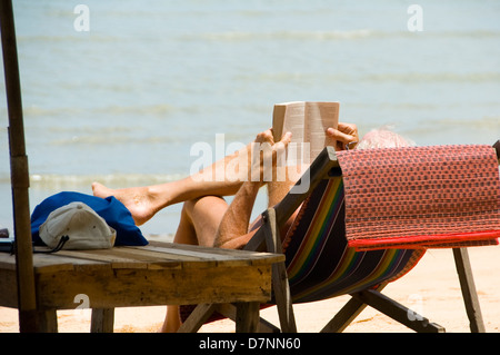 Mann liest Buch im Liegestuhl am einsamen Strand in Thailand - Hut Bang Saray - Ost-Thailand Stockfoto