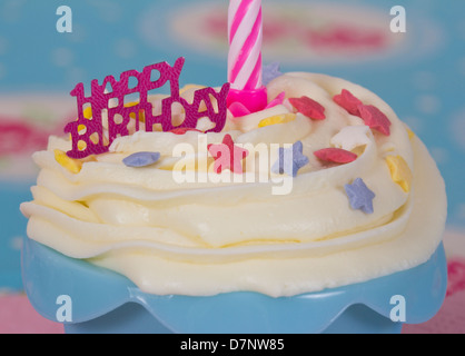 Happy Birthday Cupcake mit weißer Glasur, eine rosa Kerze und blaue Koffer Stockfoto