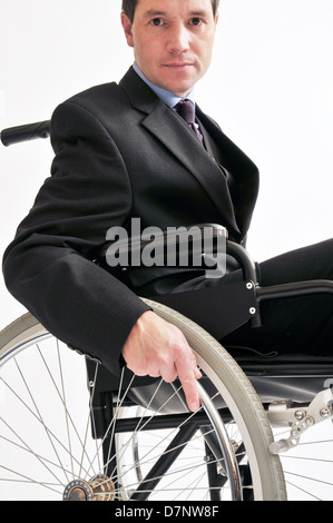 Geschäftsmann in einem dunklen Anzug, saß in einem Rollstuhl mit einem festen Griff am Lenkrad. Stockfoto