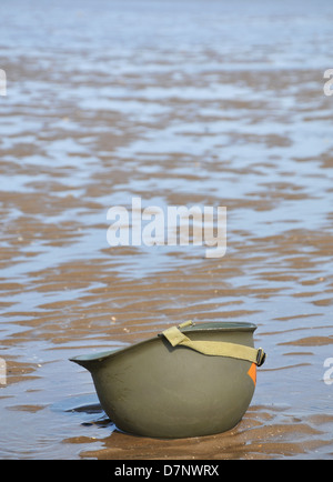 Ein amerikanischer WW2 Helm mit den Gezeiten, kopfüber am Strand sitzen. Stockfoto