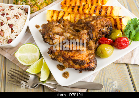 Jerk Chicken - jamaikanischen mariniert Grill Huhn serviert mit gegrillter Ananas, Reis und Erbsen und Kalk Keile. Stockfoto