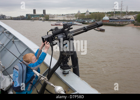 Ein kleiner Junge, zu kurz, um Punkte zu erreichen, eine Minigun-Kanone aus dem oberen Deck der HMS Illustrious über den Fluss Themse in Greenwich, London. Während die Flugzeugträger der Royal Navy am Fluss angedockt wurde, so dass die Steuern zahlenden Öffentlichkeit auf den Decks vor seiner Decommisioning tour. Navy Personal half mit dem PR-Event über die Mai Wochenende, historisch der Heimat England Flotte. Stockfoto