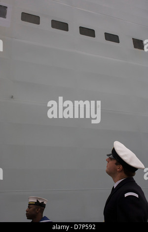 Ein Student-Offizier und ein Matrose Bewertung im Dienst unter den riesigen Rumpf ihres Schiffes während einer Tour durch die breite Öffentlichkeit an Bord Flugzeugträger der Royal Navy HMS Illustrious während eines öffentlichen Open-Tages in Greenwich. Illustrious angedockt an der Themse, so dass die Steuern zahlenden öffentlichen um den Decks vor seiner bevorstehenden Decommisioning zu erkunden. Navy Personal half mit dem PR-Event über die Mai Wochenende, historisch der Heimat England Flotte. Stockfoto