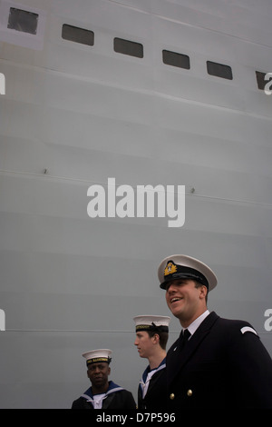 Student Offiziere und ein Matrose Bewertung im Dienst unter den riesigen Rumpf ihres Schiffes während einer Tour durch die breite Öffentlichkeit an Bord Flugzeugträger der Royal Navy HMS Illustrious während eines öffentlichen Open-Tages in Greenwich. Illustrious angedockt an der Themse, so dass die Steuern zahlenden öffentlichen um den Decks vor seiner bevorstehenden Decommisioning zu erkunden. Navy Personal half mit dem PR-Event über die Mai Wochenende, historisch der Heimat England Flotte. Stockfoto