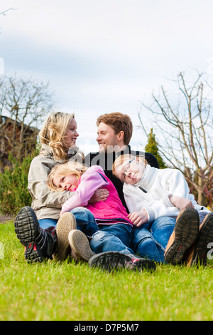 Familie, Vater, Mutter und Töchter, sitzen zusammen auf einer Wiese, sie lachen und Spaß haben Stockfoto