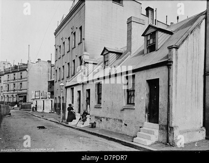 Dieses Schwarzweiß-Foto aus Nr. 41 auf der Gloucester Street in The Rocks, Sydney, zeigt eine ruhige Straßenszene mit einem Mann, der sich auf der Treppe entspannt. Das Vintage-Image zeigt den historischen Charme und das tägliche Leben in der Gegend von The Rocks. Stockfoto