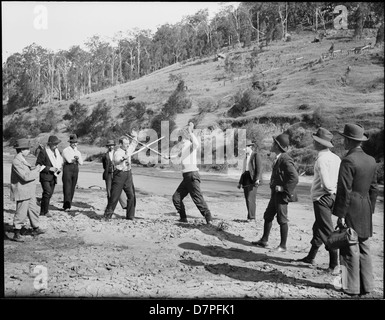 Dieses historische Foto zeigt eine Gruppe von Männern, die ein Fechtspiel beobachten, und zeigt das Interesse an Wettkampfsport und Fechten während einer bestimmten Ära. Das Bild spiegelt einen Moment des Engagements für körperliche Aktivität und geselliges Zusammenkommen wider. Stockfoto