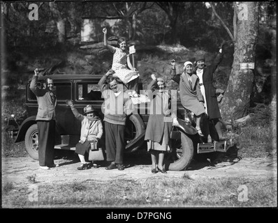 Dieses historische Schwarzweiß-Foto zeigt eine Familie, die an Palmer's Mystery Hike teilnimmt, einem Outdoor-Abenteuer aus früheren Jahren. Die Familie winkt fröhlich und sieht neben einem alten Auto auf einer malerischen Straße. Das Bild ist in der Sammlung des Powerhouse Museums erhalten und spiegelt den Geist der Familienausflüge und Freizeitaktivitäten in der Vergangenheit wider. Stockfoto
