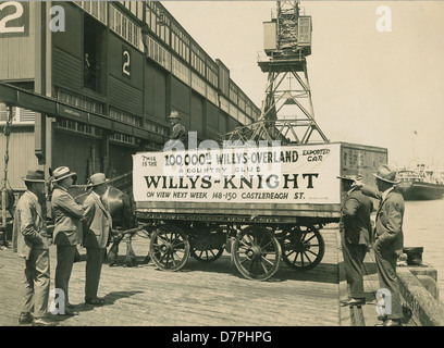Dieses Bild aus den 1920er Jahren zeigt ein Pferd und einen Wagen auf einem Kai, wobei der 100.000ste Willys-Overland-Wagen aus Australien exportiert wird. Die Szene zeigt das industrielle Wachstum und die Rolle des Verkehrs in der frühen Automobilindustrie. Stockfoto