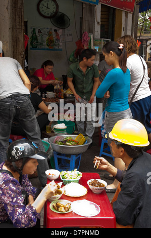 Vertikale Ansicht der Vietnamesen essen traditionelle Pho Nudeln, in Kunststoff-Tabellen auf dem Bürgersteig in Hanoi. Stockfoto