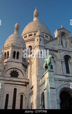 Die Fassade und die hoch aufragenden weißen Kuppeln der Basilika der Sacra-Coeur auf dem Montmartre. Über dem Portikus befindet sich eine Statue des Heiligen Ludwig. Paris, Frankreich. Stockfoto