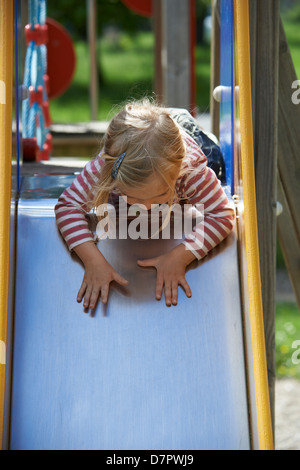 Blonde Mädchen Kind gleitende Folie auf einem Spielplatz Stockfoto