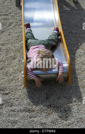 Blonde Mädchen Kind gleitende Folie auf einem Spielplatz Stockfoto