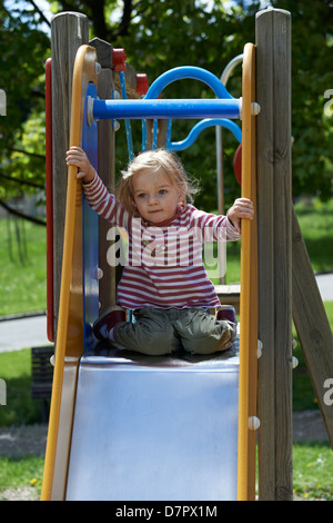 Blonde Mädchen Kind gleitende Folie auf einem Spielplatz Stockfoto