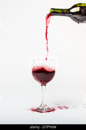 Rotwein aus der Flasche in ein Glas gießen und spritzt den weißen Hintergrund. Stockfoto