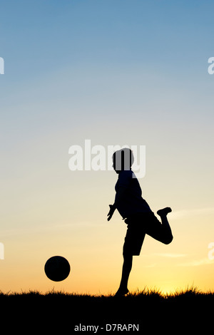 Jungen spielen mit einem Fußball bei Sonnenuntergang. Silhouette Stockfoto