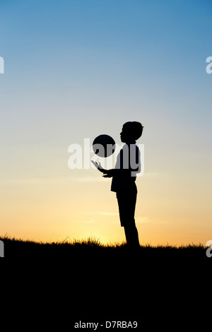Jungen spielen mit einem Fußball bei Sonnenuntergang. Silhouette Stockfoto