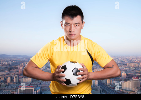 Fußballspieler mit Ball, Brust, Stadtbild Hintergrund Stockfoto