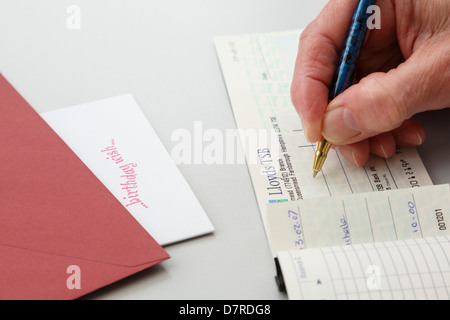 Senior weiblichen Rentner schreiben einen Scheck von Lloyds TSB als Geschenk zu einem Geburtstag Grußkarte zulegen. England, UK, Großbritannien. Stockfoto