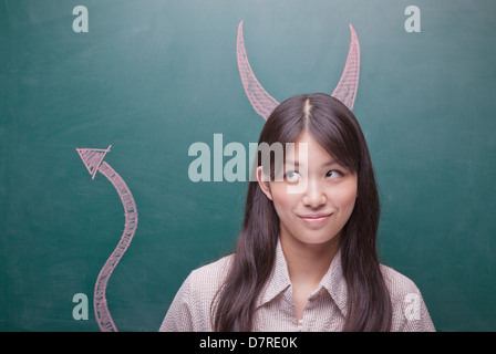 Junge Frau mit Teufelshörnern und Tail an Tafel Stockfoto