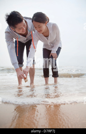 Junges Paar Blick auf Muscheln am Strand Stockfoto