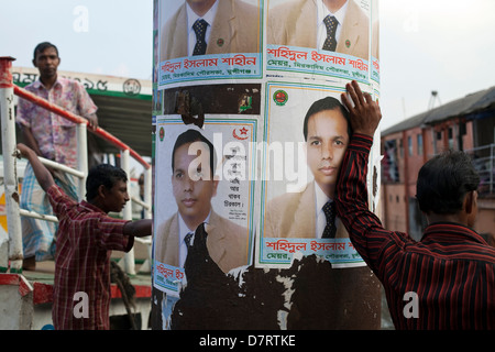 Ein Mann wartet am Kai für eine Fähre nach andocken und lehnt sich auf politische Plakate, Sadarghat Fährhafen, Dhaka, Bangladesch Stockfoto