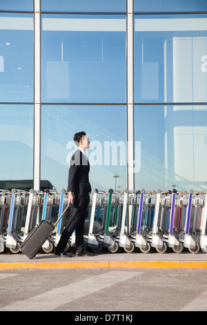 Reisende mit Koffer neben Zeile der Gepäckwagen am Flughafen Stockfoto