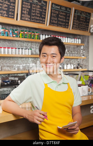 Porträt von lächelnden jungen Barista mit Block und Stift, Coffee-Shop, Peking Stockfoto