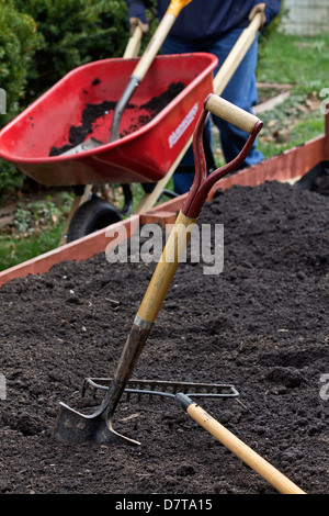Der Gärtner schiebt das Laufrad mit Erde und die Schaufel im Garten