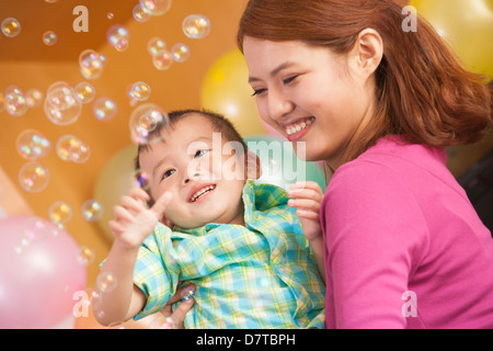 Mutter, die kleinen Jungen zu halten, während er mit Bubbles spielt Stockfoto