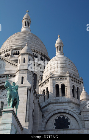 Die hoch aufragenden weißen Kuppeln der Basilika Sacré-Coeur auf dem Montmartre. Über dem Portikus steht ein Reiterstandbild der Jeanne d ' Arc. Paris, Frankreich. Stockfoto