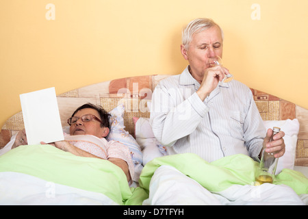 Älteres paar entspannen Sie sich im Bett mit Alkohol und Buch Stockfoto