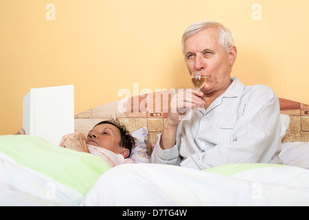 Älteres Paar im Bett trinken Alkohol und Buch Stockfoto