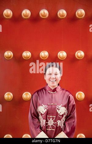 Reife Frau in traditioneller Kleidung stehen neben traditionellen chinesischen Tür Stockfoto