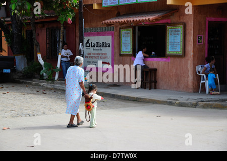 Frau und Kind mit Rucksack Kreuzung Straße in San Pancho, Mexiko. Stockfoto