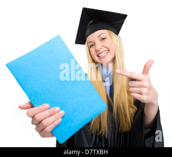 Lächelnde junge Frau in Graduierung Kleid zeigt auf Buch Stockfoto