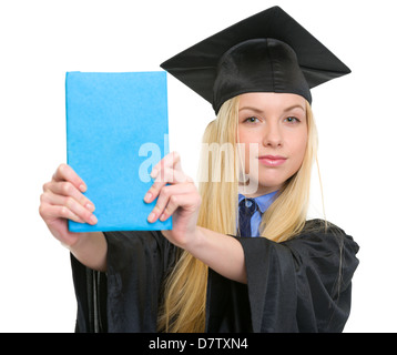 Junge Frau in Graduierung Kleid zeigt Buch Stockfoto