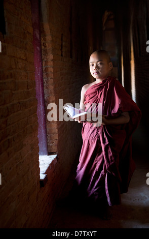 Buddhistischer Novize lesen buddhistische Schriften vor dem Hintergrund eines Fensters in einem der vielen Tempel von Bagan, Birma Stockfoto