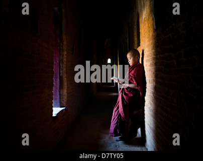 Buddhistischer Novize lesen buddhistische Schriften vor dem Hintergrund eines Fensters in einem der vielen Tempel von Bagan, Birma Stockfoto