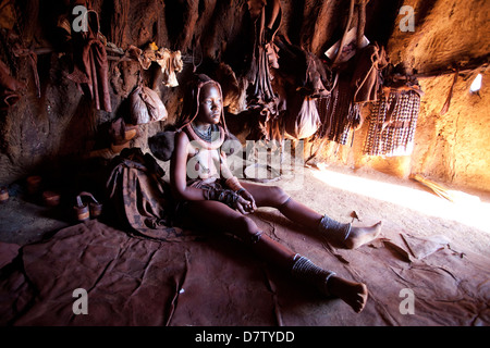 Himba Frau in einer Schlamm-Wohnung Hütte tragen Kleidung und Schmuck und bedeckt in Otjize, Kunene-Region, Kaokoland, Namibia Stockfoto