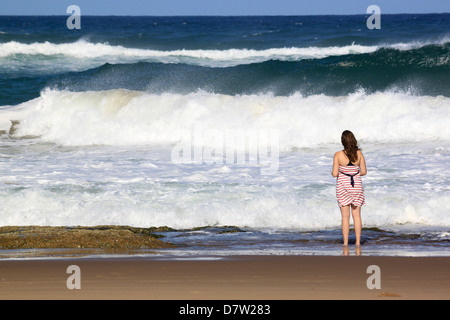 Eine junge Frau steht von brechenden Wellen am Strand, St. Lucia Wetlands, Kwa-Zulu Natal, Südafrika Stockfoto