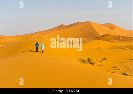 Zwei Berber Männer gehen in den Sanddünen des Erg Chebbi Wüste Sahara in der Nähe von Merzouga, Marokko, Nordafrika Stockfoto